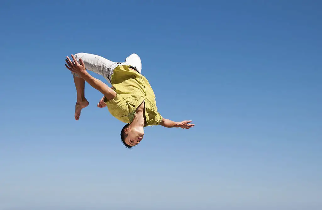 Young man doing a somersault on the background of blue sky