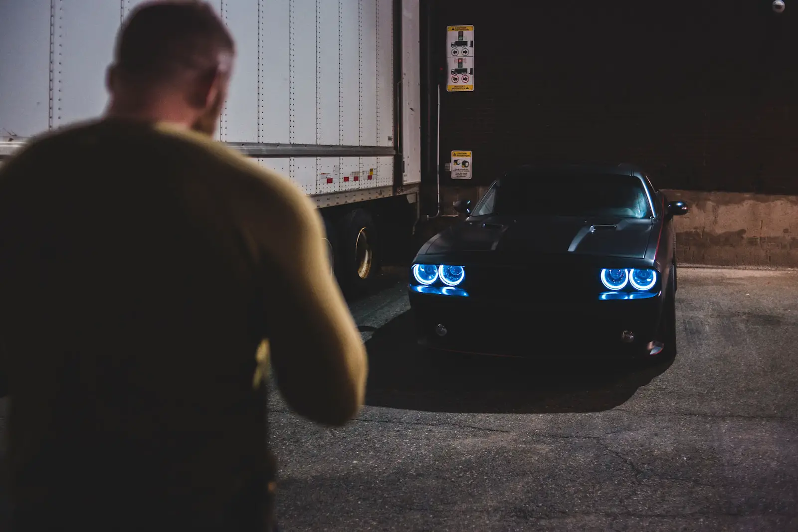man in black t-shirt standing beside blue car during nighttime